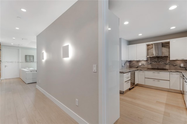 kitchen with light wood-type flooring, white cabinets, wall chimney range hood, and decorative backsplash