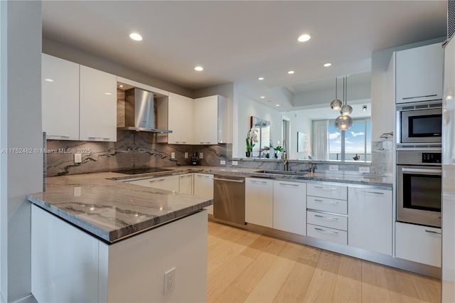 kitchen featuring wall chimney range hood, white cabinetry, stainless steel appliances, and a sink