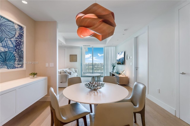 dining area with light wood-style floors, recessed lighting, a raised ceiling, and baseboards