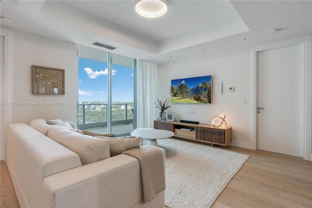 living room featuring light wood-style flooring, floor to ceiling windows, visible vents, and a tray ceiling