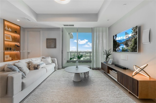 living room with a tray ceiling, visible vents, and expansive windows