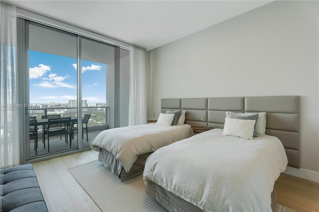 bedroom with expansive windows, access to outside, light wood-type flooring, and baseboards