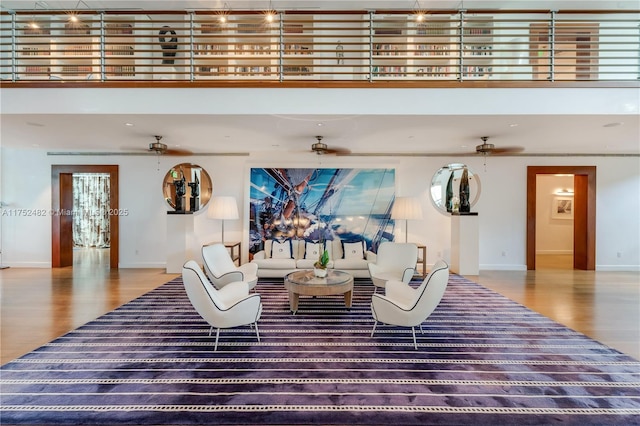 living area featuring ceiling fan, wood finished floors, a towering ceiling, and baseboards