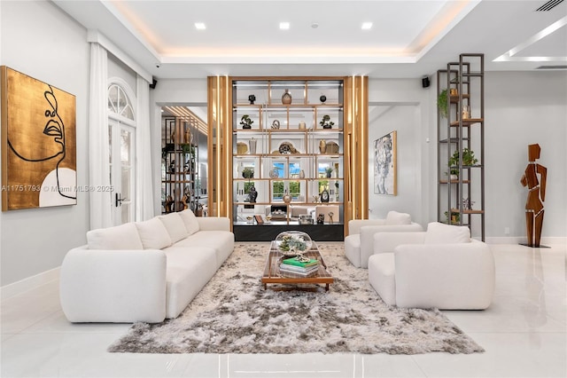 living area with a tray ceiling, light tile patterned flooring, visible vents, and baseboards