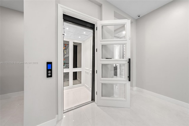 hall featuring elevator, baseboards, and light tile patterned flooring