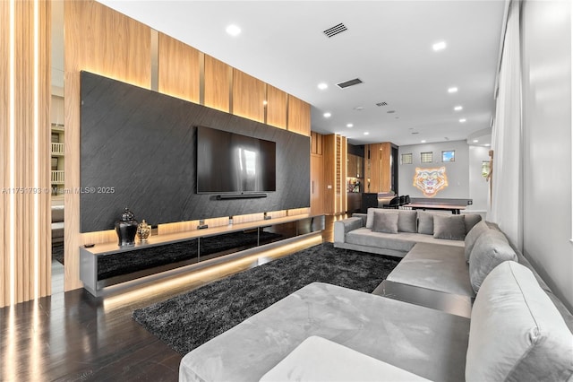 living area with an accent wall, dark wood-style flooring, visible vents, and recessed lighting