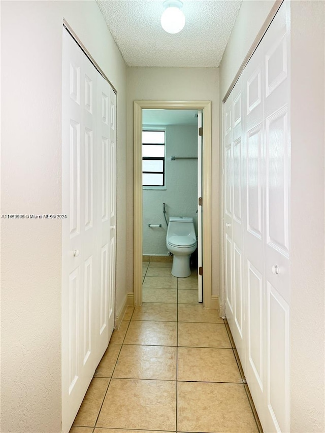 hall featuring light tile patterned floors, baseboards, and a textured ceiling