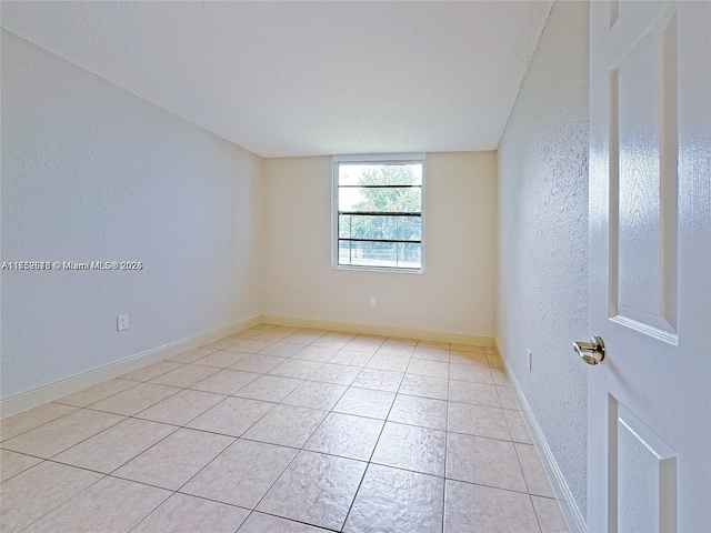 unfurnished room with a textured wall, a textured ceiling, baseboards, and light tile patterned floors