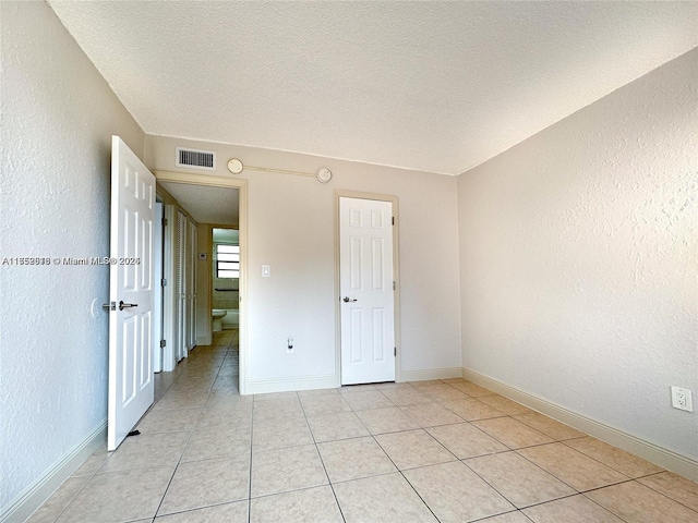 empty room featuring baseboards, visible vents, a textured wall, a textured ceiling, and light tile patterned flooring