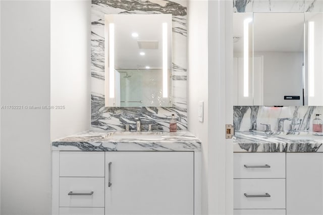 full bath featuring a stall shower, two vanities, decorative backsplash, and a sink