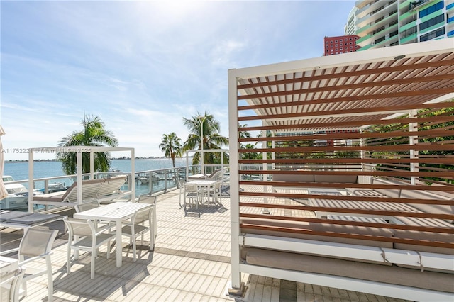 wooden deck with outdoor dining area, a water view, and a pergola