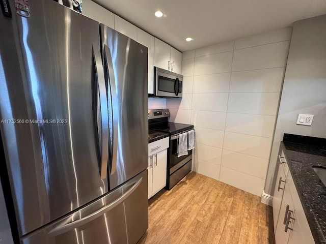 kitchen featuring dark stone countertops, stainless steel appliances, light wood-style floors, white cabinetry, and tile walls