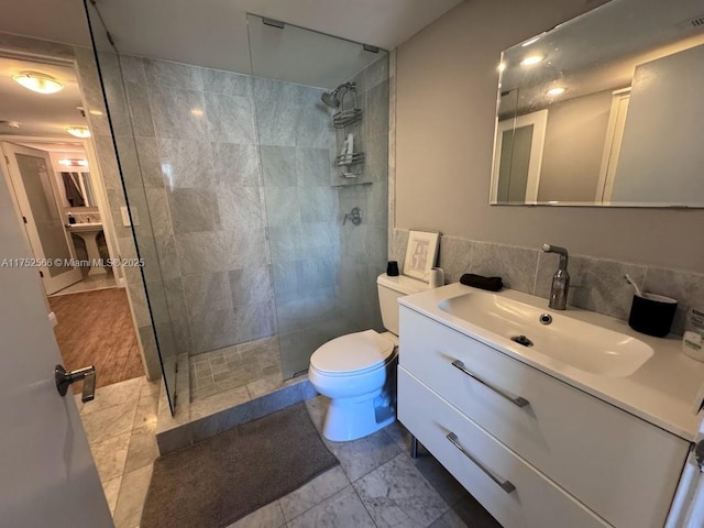 bathroom with toilet, tile walls, tiled shower, and vanity