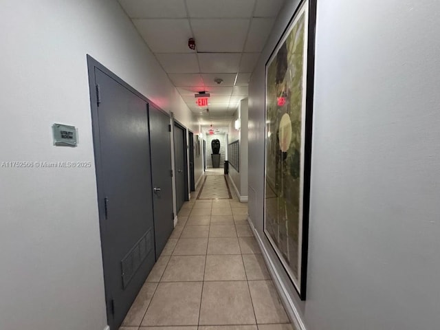 corridor featuring light tile patterned floors, baseboards, and a drop ceiling