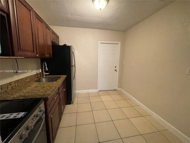 kitchen featuring light tile patterned floors, baseboards, a textured ceiling, stainless steel range with electric stovetop, and a sink