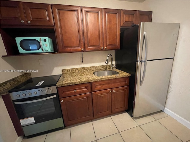 kitchen featuring electric range, dark stone countertops, freestanding refrigerator, a sink, and light tile patterned flooring