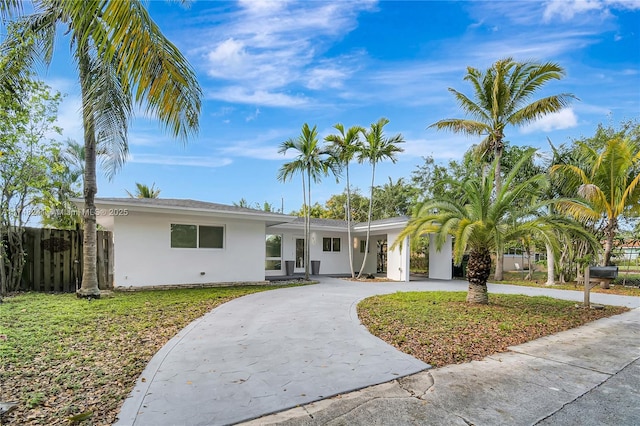 view of front of home featuring stucco siding, fence, and curved driveway
