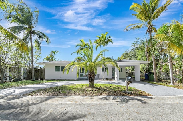 view of front facade featuring a carport, curved driveway, fence, and stucco siding