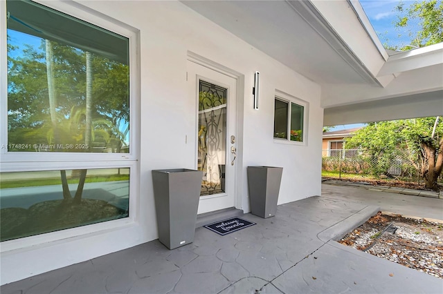 entrance to property featuring stucco siding and fence