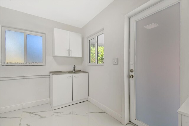 interior space featuring baseboards, a sink, light countertops, white cabinets, and marble finish floor