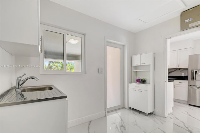 kitchen featuring baseboards, a sink, stainless steel refrigerator with ice dispenser, white cabinetry, and marble finish floor