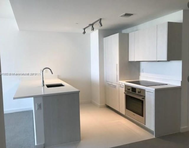 kitchen with light countertops, a sink, oven, and black electric cooktop