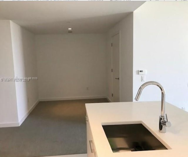 kitchen featuring dark carpet, light countertops, a sink, and baseboards