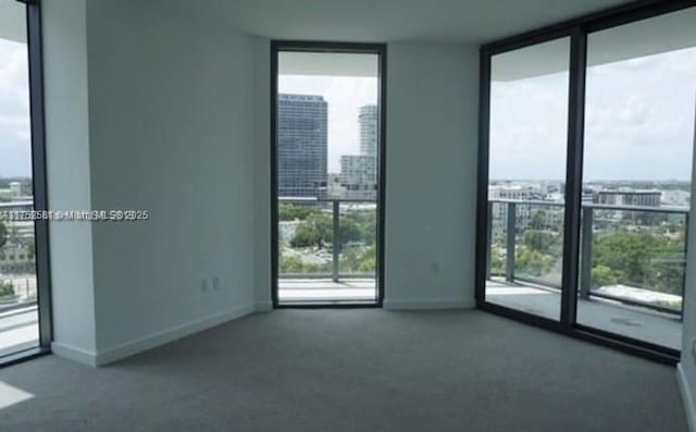 empty room featuring baseboards, floor to ceiling windows, carpet flooring, and a city view