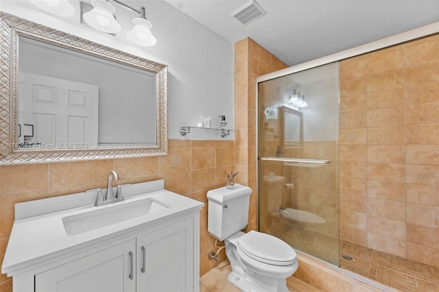 full bath featuring toilet, vanity, visible vents, tile walls, and a stall shower