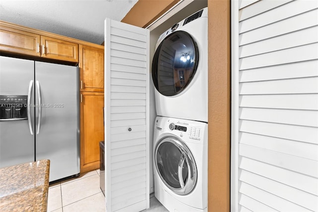 clothes washing area featuring light tile patterned floors, laundry area, and stacked washer and clothes dryer