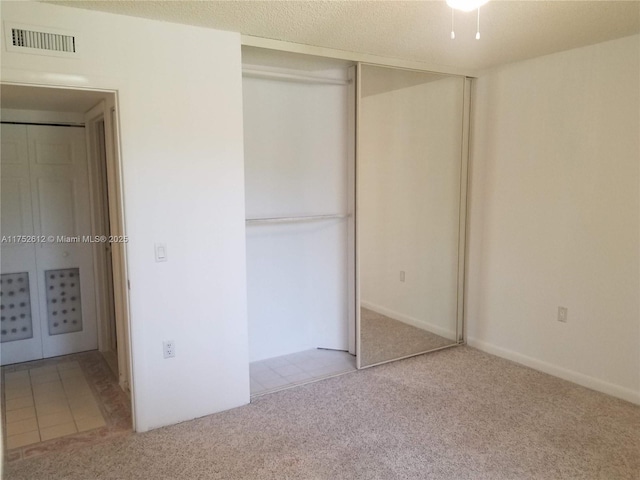 unfurnished bedroom featuring a textured ceiling, a closet, visible vents, and light colored carpet