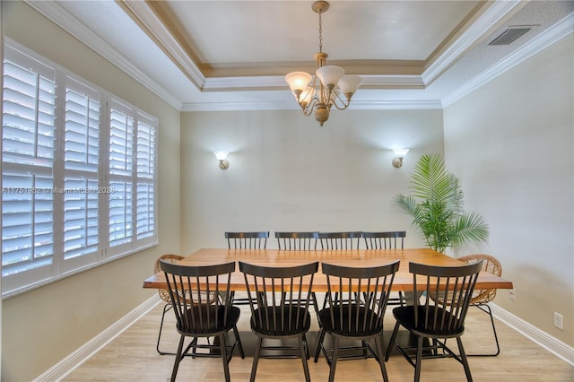 dining space with light wood-type flooring, a tray ceiling, and visible vents