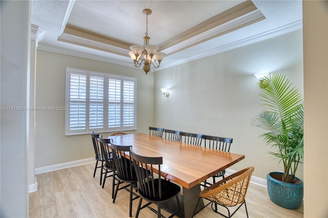 dining room with a chandelier, baseboards, light wood-type flooring, a raised ceiling, and crown molding