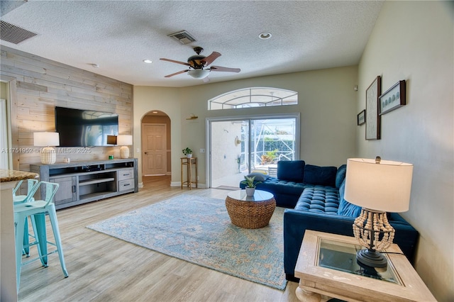 living room with light wood-type flooring, visible vents, arched walkways, and a textured ceiling