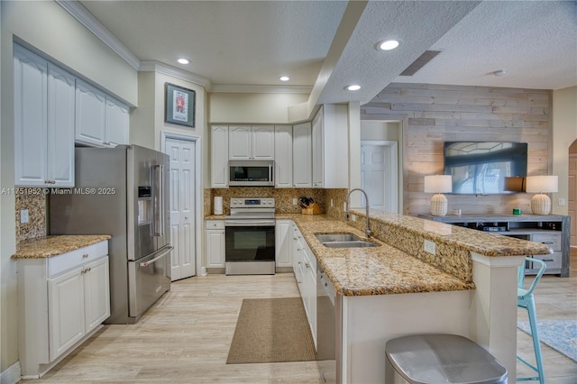 kitchen with light stone counters, a kitchen breakfast bar, a peninsula, stainless steel appliances, and a sink