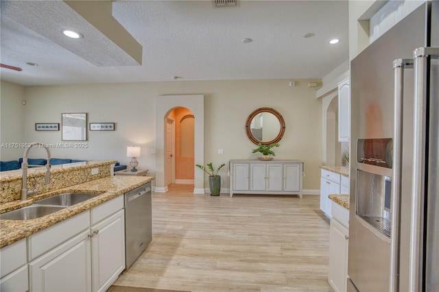 kitchen featuring arched walkways, stainless steel appliances, a sink, white cabinetry, and light wood finished floors