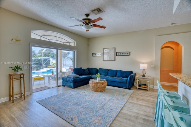 living area featuring baseboards, visible vents, a ceiling fan, a textured ceiling, and light wood-style floors