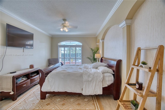 bedroom with arched walkways, crown molding, light wood-style flooring, a ceiling fan, and a textured ceiling