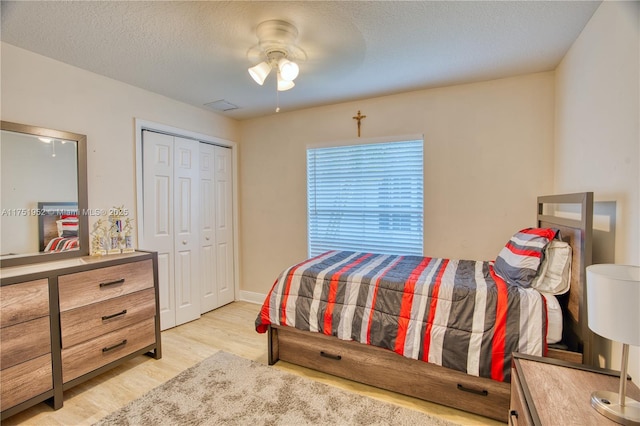 bedroom with a textured ceiling, visible vents, a ceiling fan, a closet, and light wood-type flooring