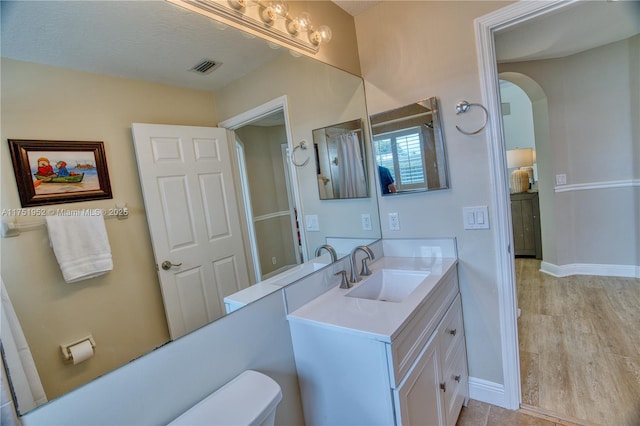 bathroom featuring toilet, wood finished floors, vanity, visible vents, and baseboards