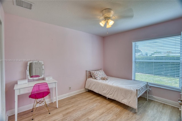 bedroom featuring a textured ceiling, a ceiling fan, visible vents, baseboards, and light wood finished floors