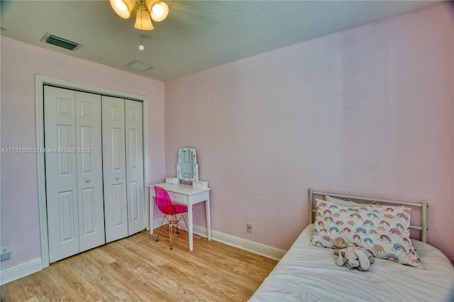 bedroom featuring visible vents, baseboards, light wood-style flooring, a textured ceiling, and a closet