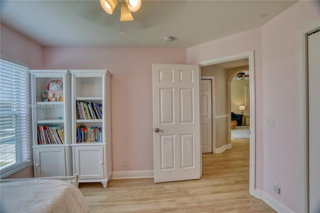 bedroom with light wood-style floors, arched walkways, a textured ceiling, and baseboards