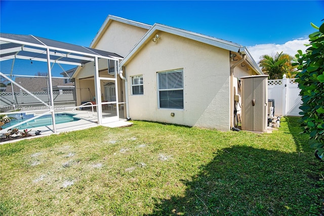 rear view of house with glass enclosure, fence, a lawn, a fenced in pool, and stucco siding