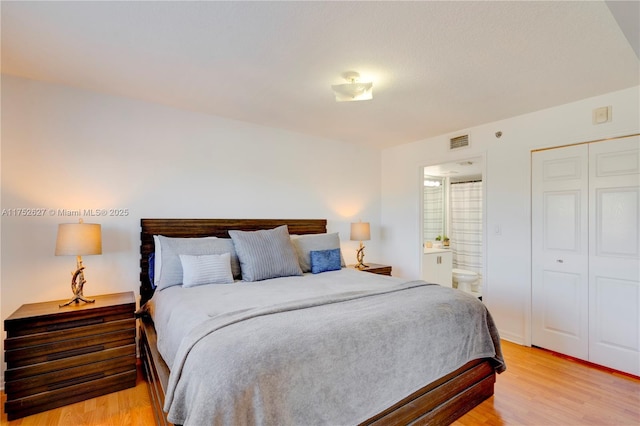 bedroom featuring light wood-type flooring, visible vents, and ensuite bath