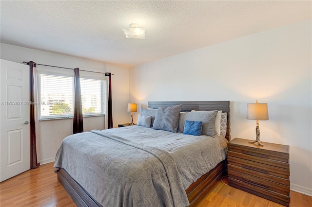 bedroom featuring light wood-type flooring, baseboards, and a textured ceiling