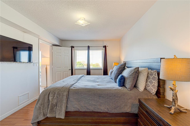 bedroom with visible vents, a textured ceiling, baseboards, and wood finished floors