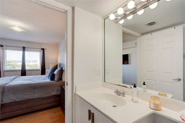 ensuite bathroom featuring visible vents, connected bathroom, wood finished floors, a textured ceiling, and vanity