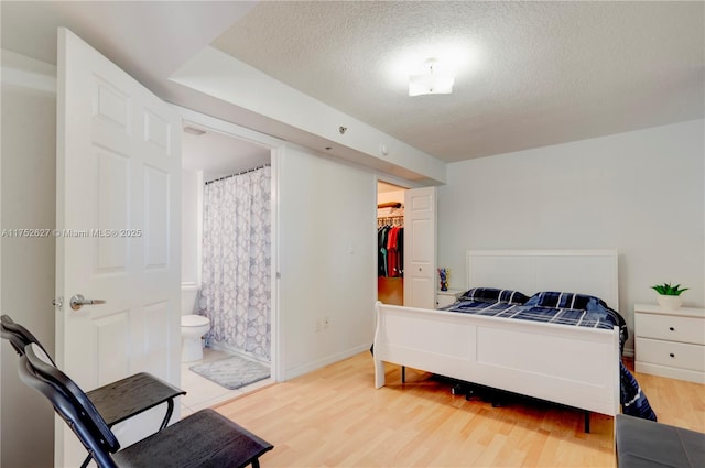 bedroom with a textured ceiling, ensuite bathroom, wood finished floors, baseboards, and a spacious closet