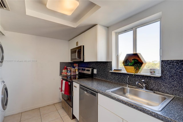 kitchen with stainless steel appliances, a sink, white cabinets, stacked washing maching and dryer, and dark countertops